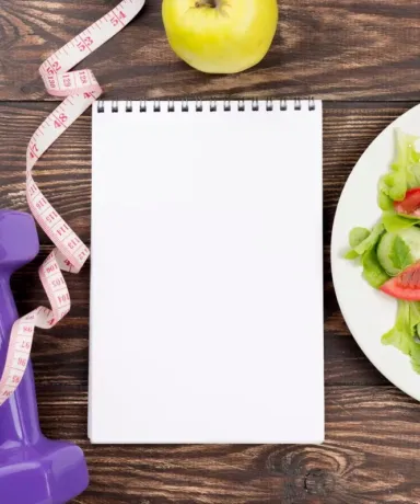 Ensalada junto a una libreta, una mancuerna y una manzana