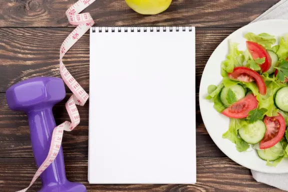 Ensalada junto a una libreta, una mancuerna y una manzana